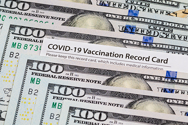 A row of $100 bills with a COVID-19 vaccination card peeking out between them.