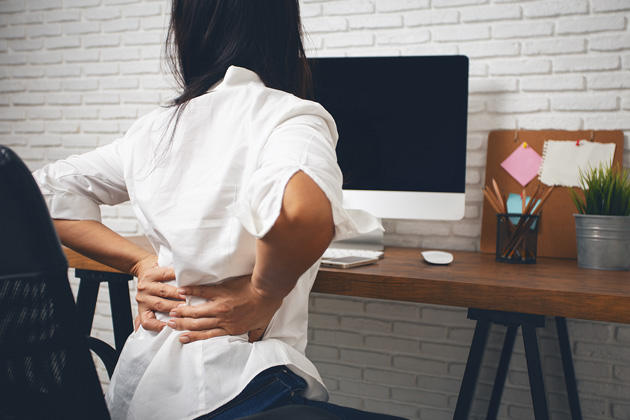 Woman sitting in front of computer grasping her back in pain.