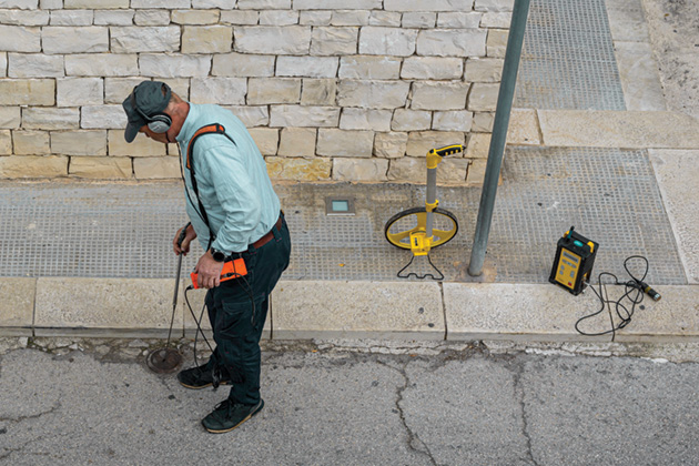 Man placing water-detecting sensor outside building.