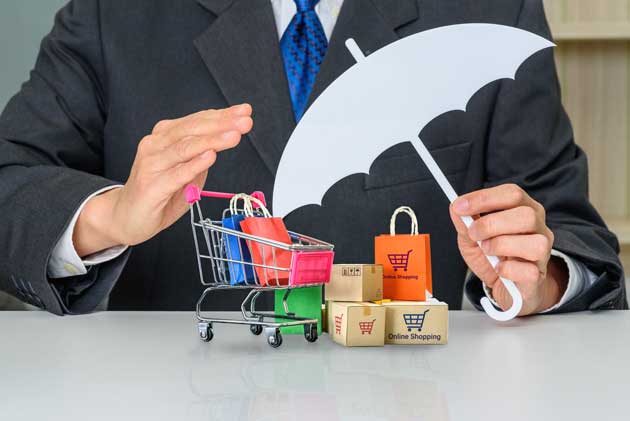 Person in a suit holding an umbrella over a miniature shopping cart and bags.
