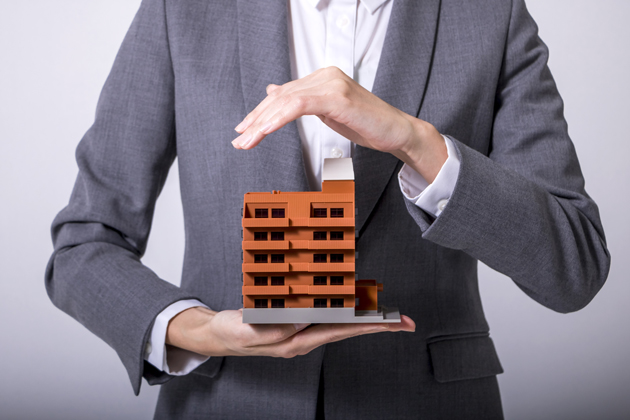 Person shielding a small building with his hand.