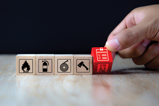 Five wooden cubes in a row, each with a logo on it: 1. a flame, 2. a fire extinguisher, 3. a hose, 4. an axe, and the fifth cube is red with a picture of a clipboard and a paper that says 