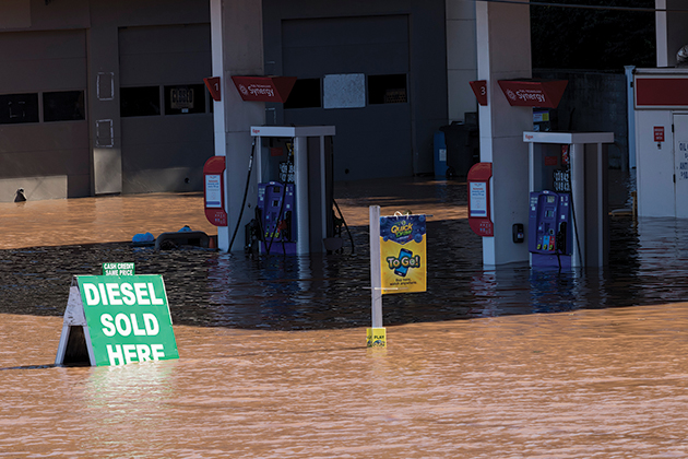 A photo of a flooded gas station, with the water halfway up the gas pumps and a sign in the water that says 