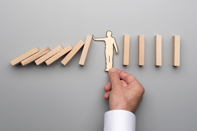 A paper figure of a person holding up their hand to prevent wooden blocks from toppling in a row.