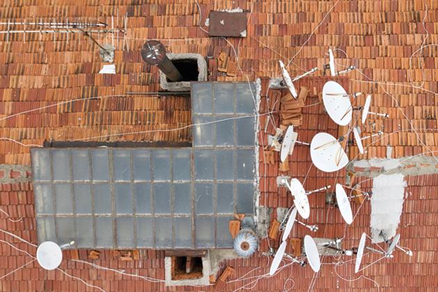 A red-shingled house roof with a skylight and multiple satellite dishes.