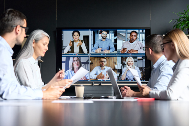 Several people around a conference table meet with people on a teleconference.