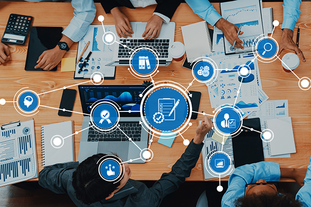 People working at a table with documents, laptops and graphs, overlaid with digital icons representing business processes, teamwork, and data analysis